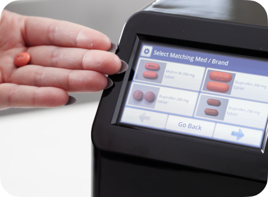 Hand holding a pill and the MedaCube screen displaying four similar looking pills that are in the database. 