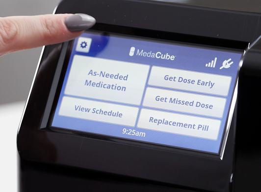 The MedaCube screen with a finger pointing to the caregiver menu button. 